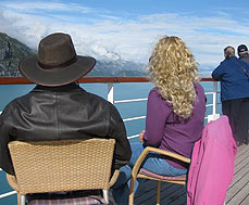 couple sit on deck on cruise ship looking at Alaska shoreline
